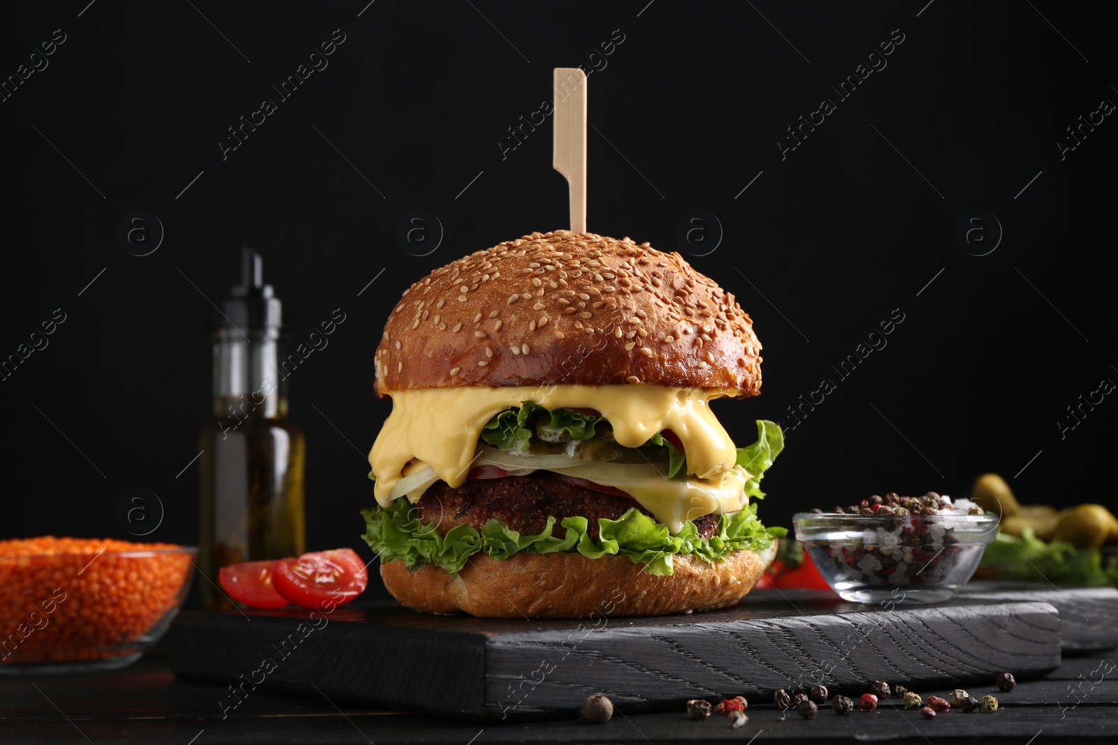 Photo of Tasty vegetarian burger and ingredients on black wooden table