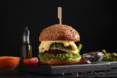 Photo of Tasty vegetarian burger and ingredients on black wooden table