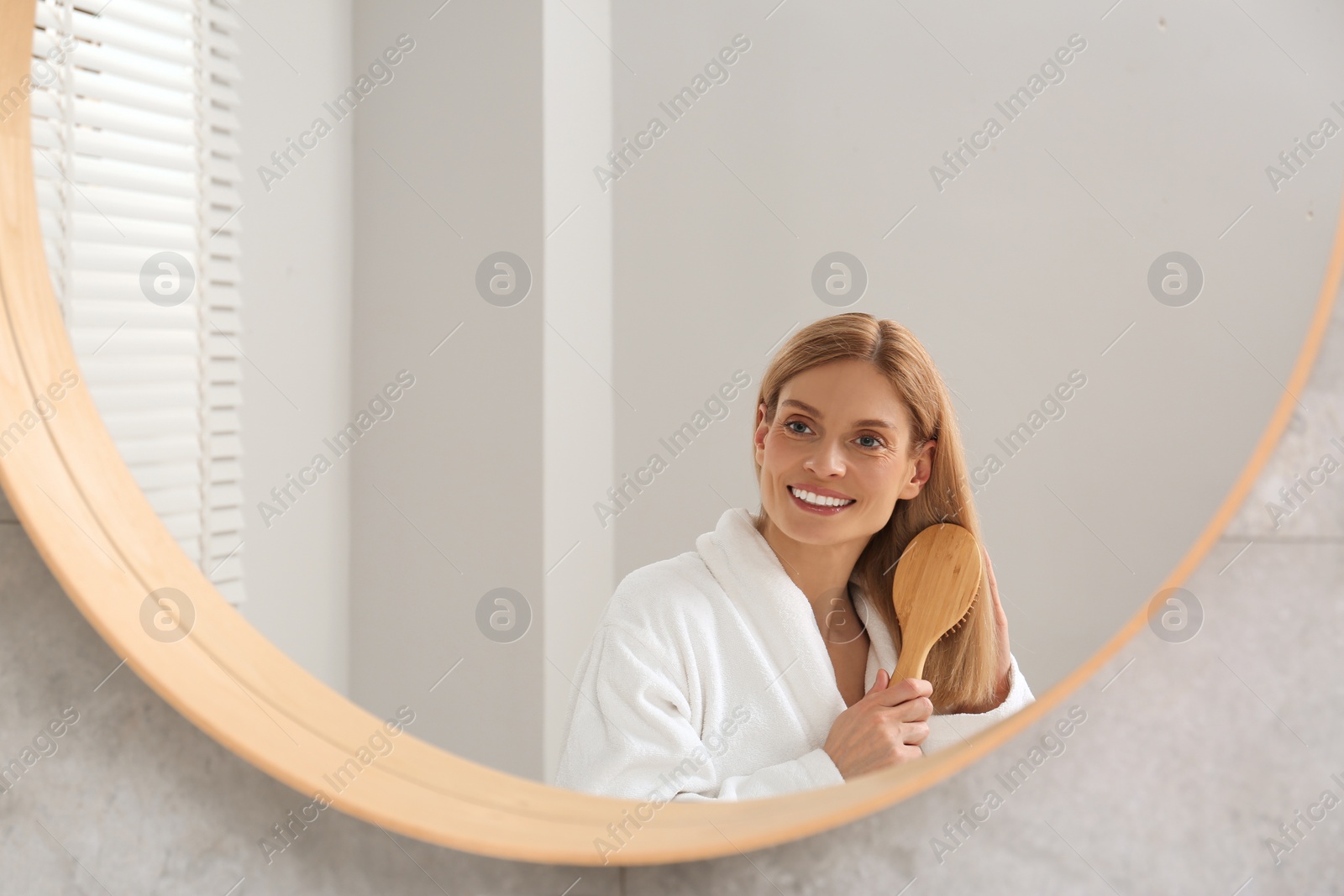 Photo of Beautiful woman brushing her hair near mirror in bathroom