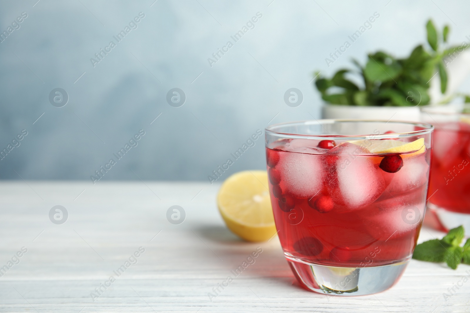 Photo of Tasty refreshing cranberry cocktail with lemon on white wooden table, closeup. Space for text