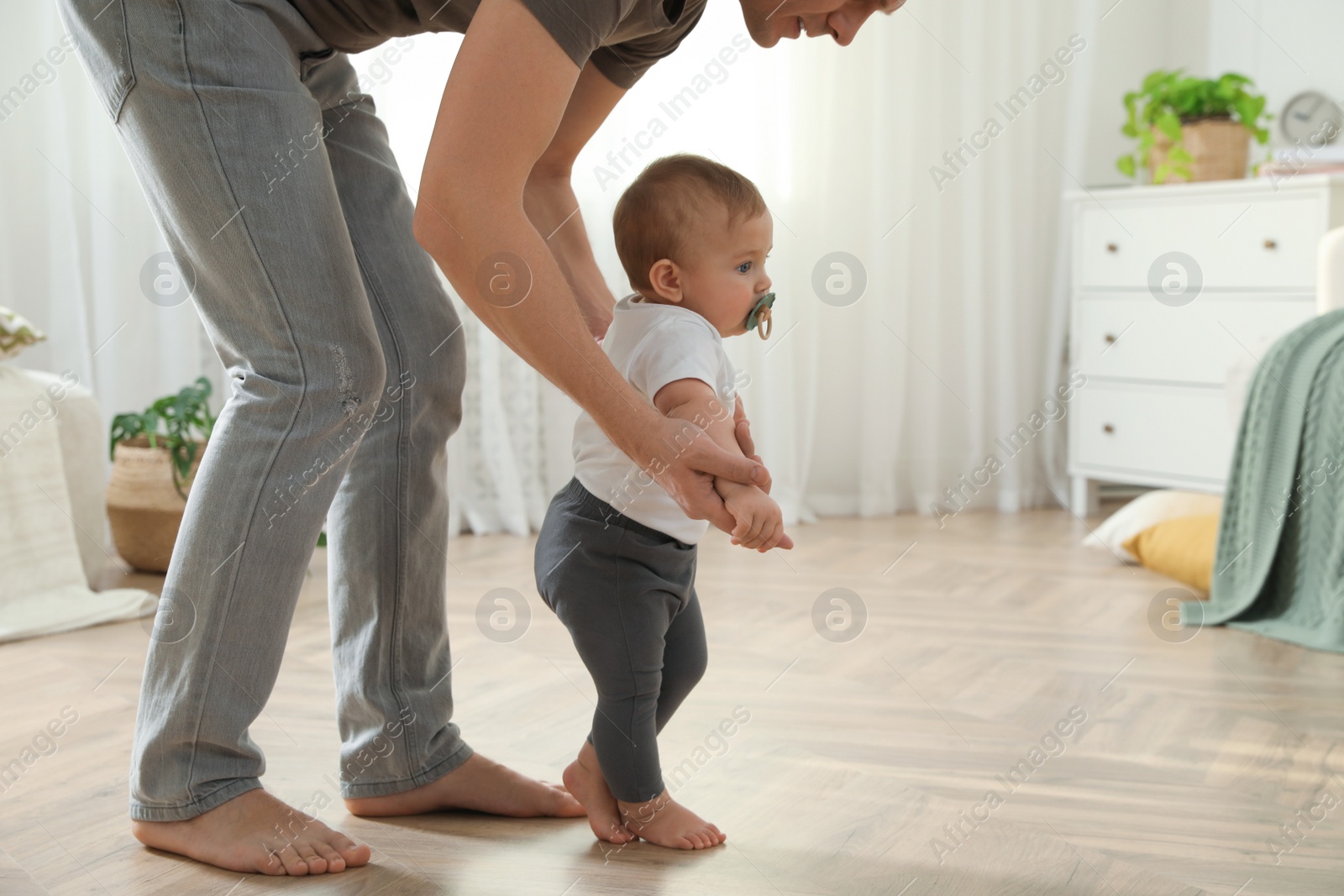 Photo of Father supporting his baby daughter while she learning to walk at home