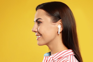 Happy young woman listening to music through wireless earphones on yellow background