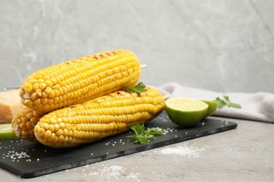 Delicious grilled corn cobs on grey table. Space for text