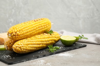 Photo of Delicious grilled corn cobs on grey table. Space for text