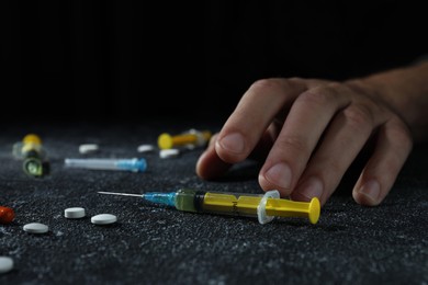 Addicted man and different hard drugs on black textured table, closeup