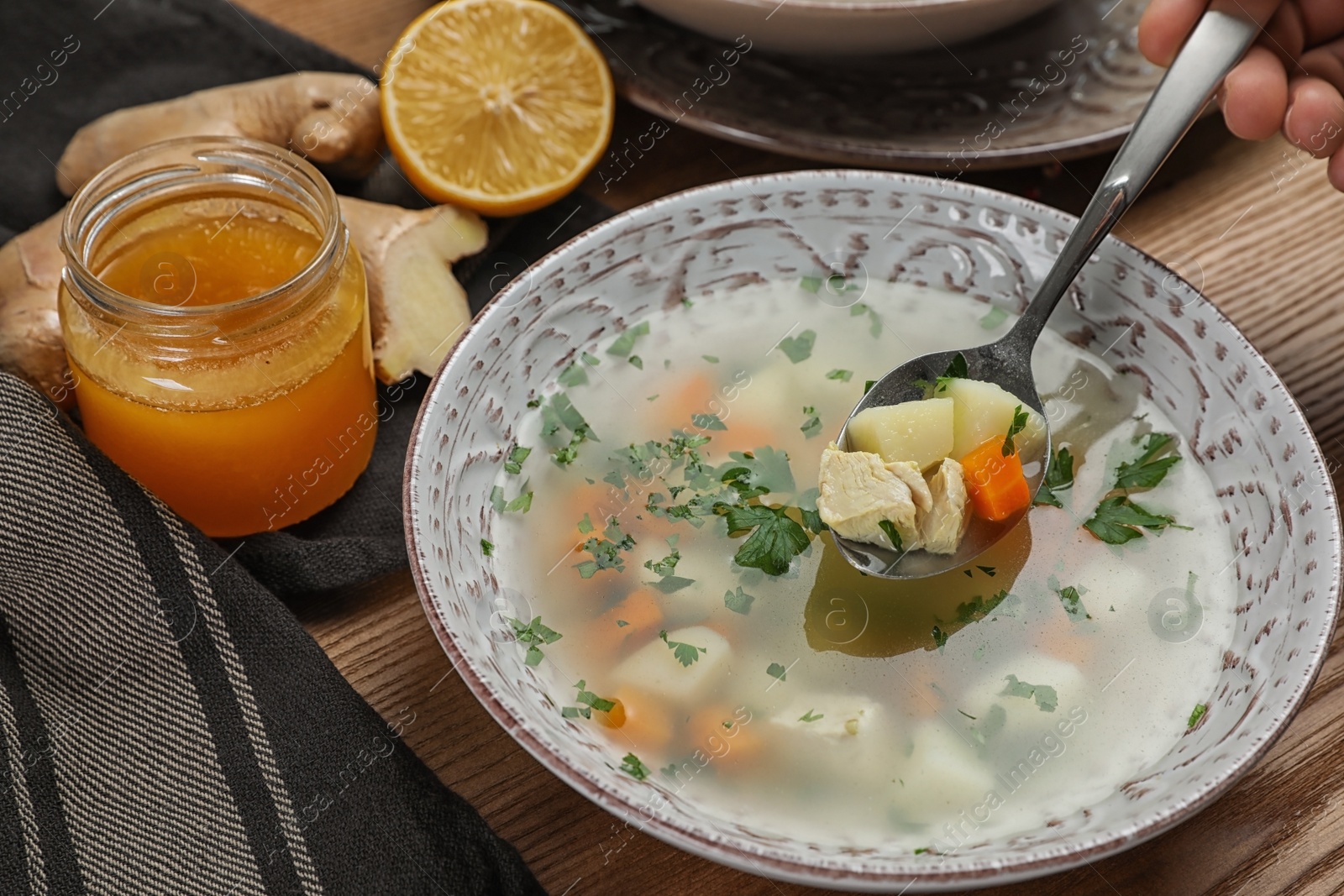 Photo of Spoon with fresh homemade soup to cure flu over bowl on wooden table