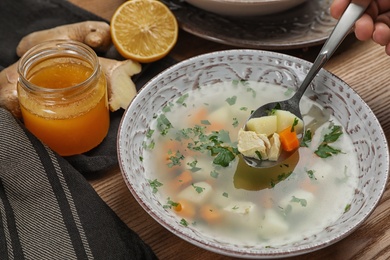 Spoon with fresh homemade soup to cure flu over bowl on wooden table