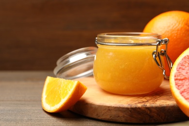 Photo of Delicious orange marmalade in jar and fresh fruits on wooden table, closeup. Space for text