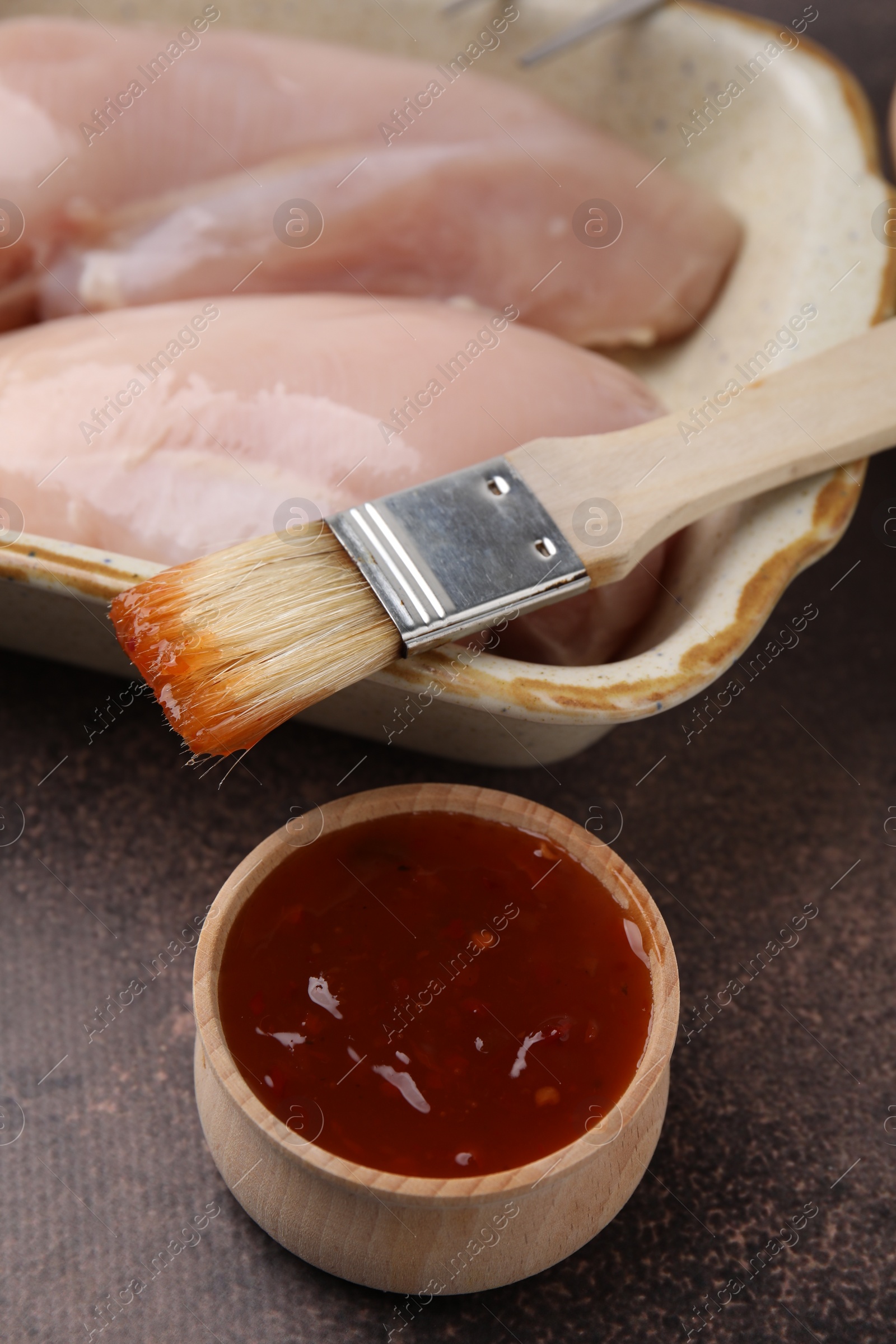 Photo of Marinade, basting brush and raw chicken fillets on brown table, closeup