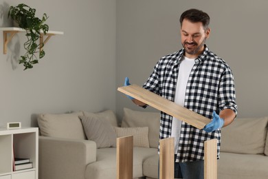 Man assembling wooden furniture in living room. Space for text
