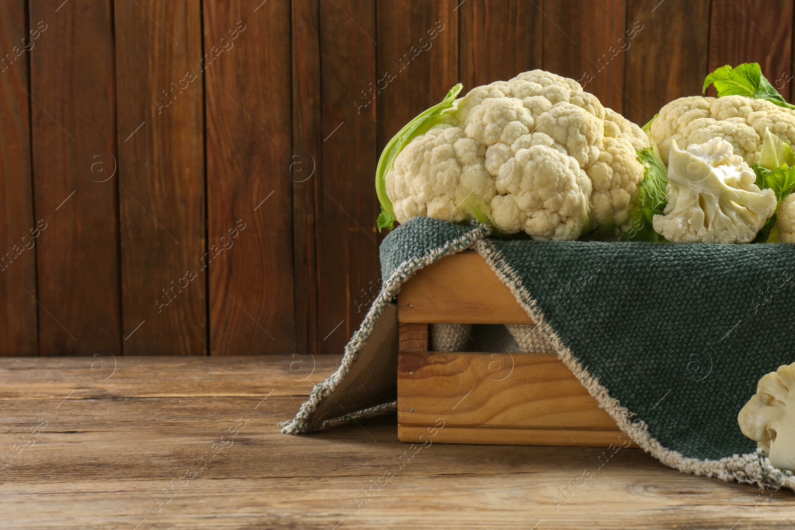 Photo of Crate with cut and whole cauliflowers on wooden table. Space for text