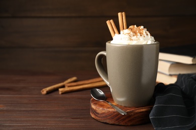 Photo of Cup of hot drink with aromatic cinnamon and whipped cream on wooden table. Space for text