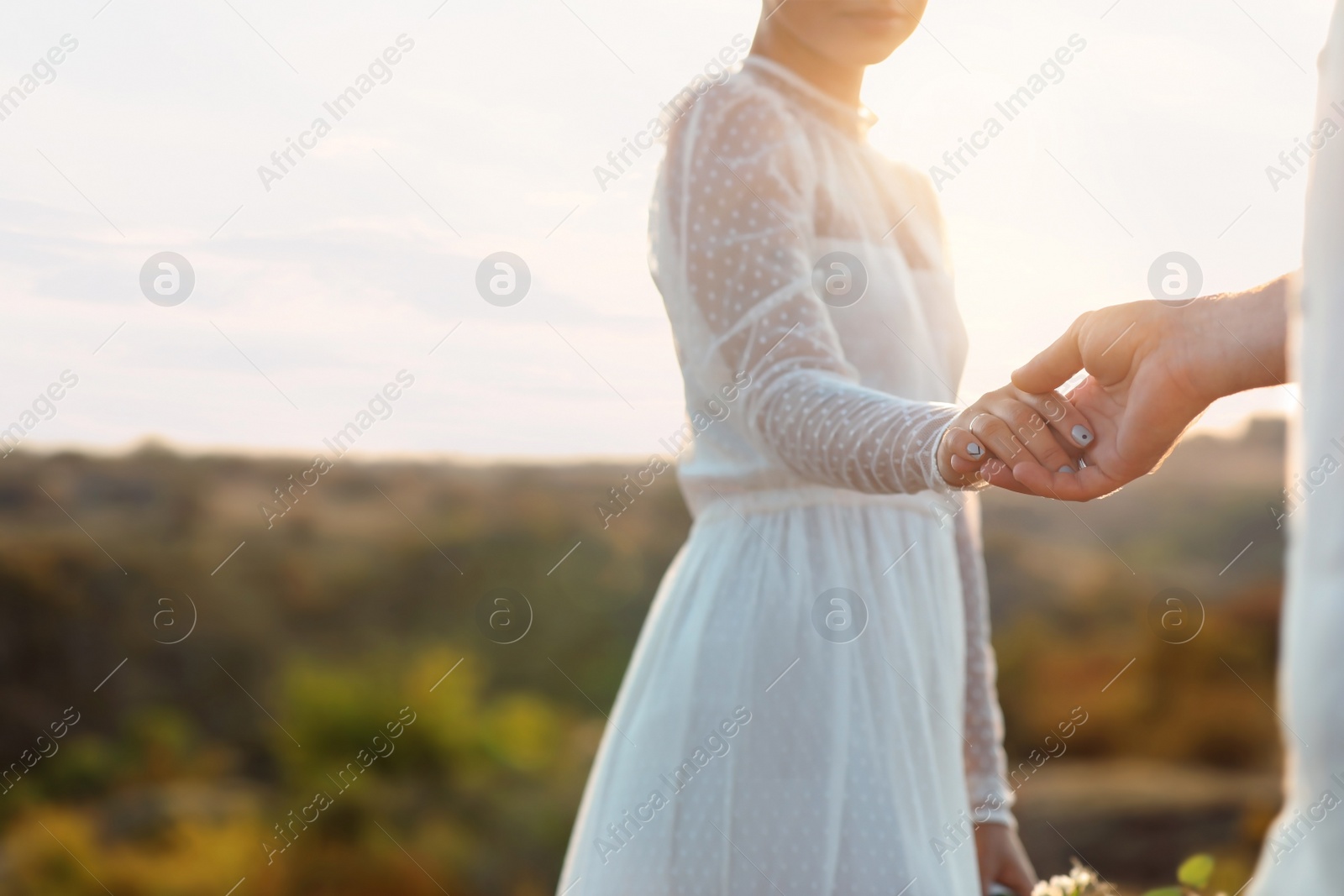 Photo of Happy bride and groom holding hands outdoors, closeup
