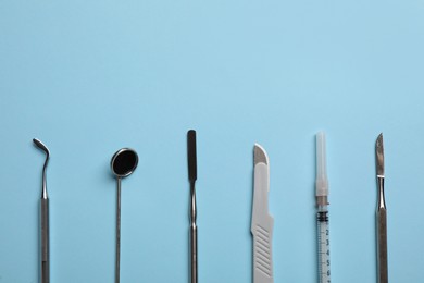 Photo of Set of different dentist's tools and syringe on light blue background, flat lay. Space for text