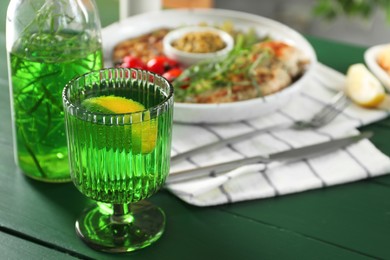 Photo of Delicious drink with tarragon in glass on green table, closeup. Space for text