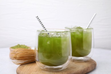 Delicious iced green matcha tea and bamboo whisk on white table, closeup