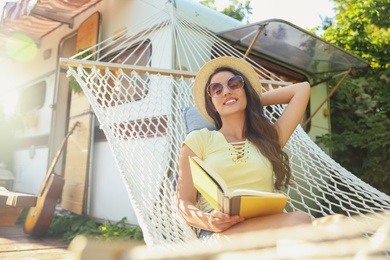 Photo of Young woman with book resting in hammock near motorhome outdoors on sunny day