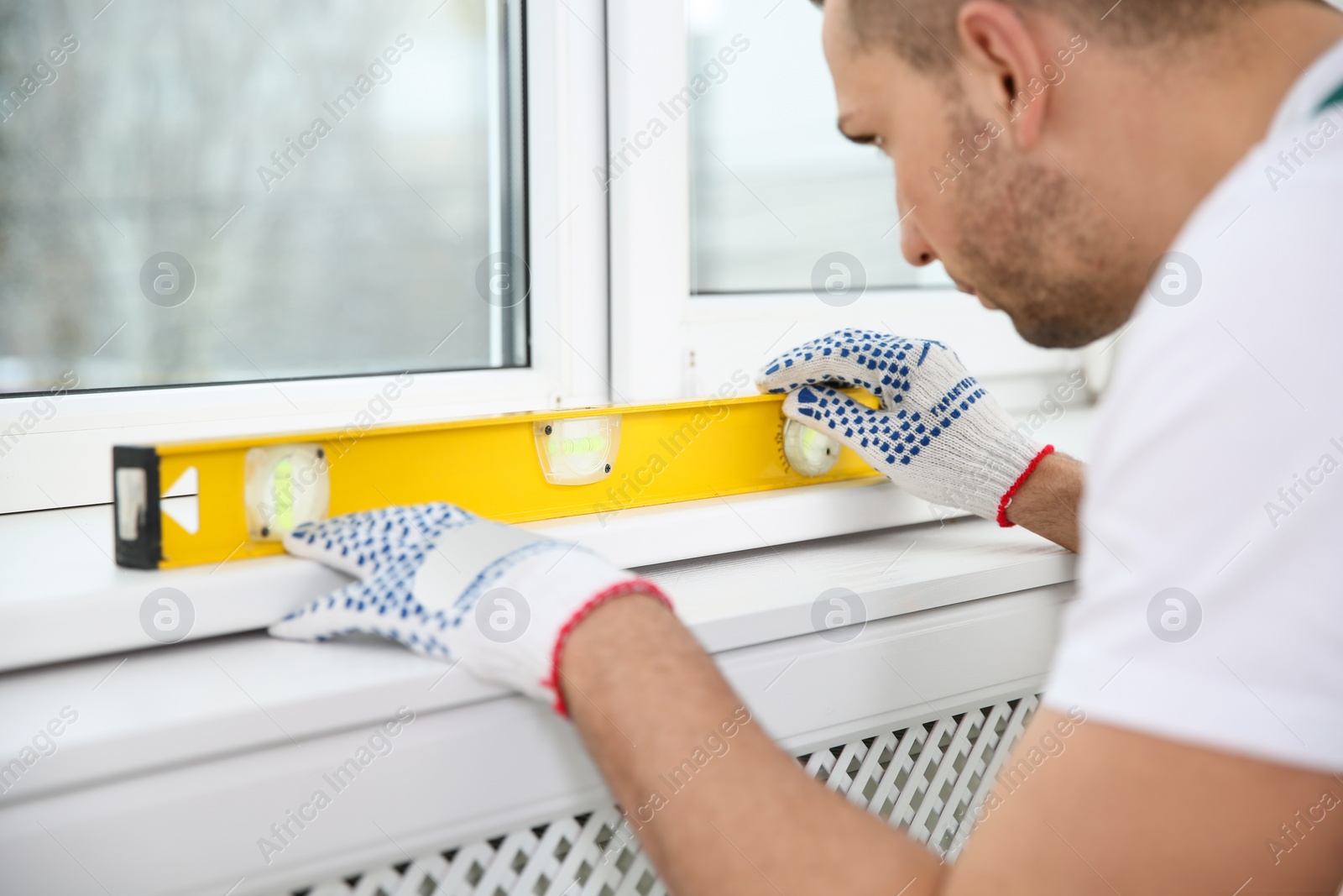 Photo of Construction worker using bubble level while installing window indoors