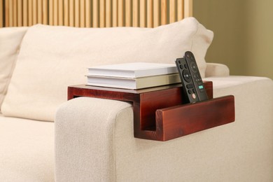 Photo of Books and remote controls on sofa armrest wooden table in room. Interior element