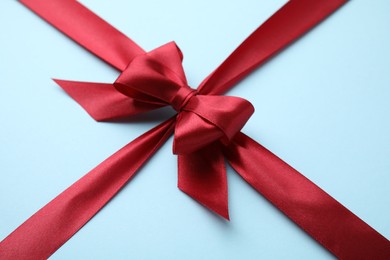 Photo of Red satin ribbon with bow on light blue background, closeup