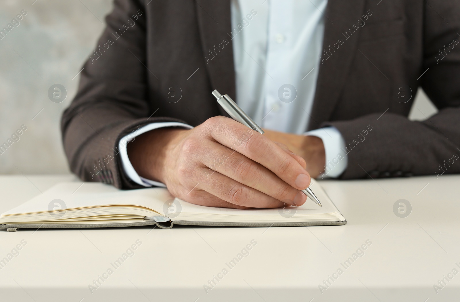 Photo of Man writing in notebook at white table, closeup