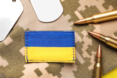 Photo of Military ID tags near Ukrainian army patch and bullets on camouflage background, flat lay