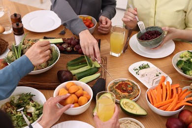 Photo of Friends eating vegetarian food at wooden table indoors, closeup