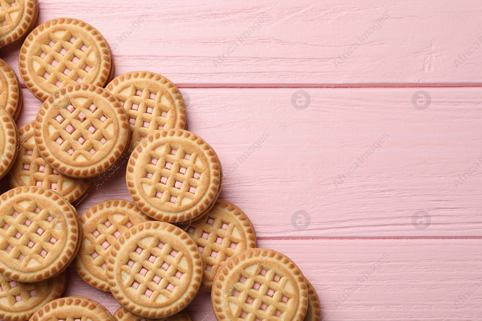 Photo of Tasty sandwich cookies with cream on pink wooden table, flat lay. Space for text