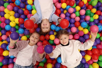 Photo of Happy little kids lying on many colorful balls, top view