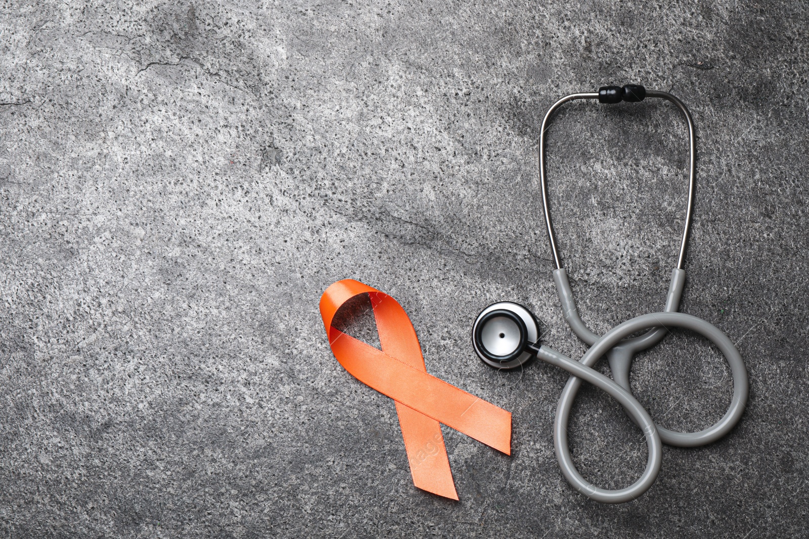 Photo of Orange ribbon and stethoscope on grey table, flat lay with space for text. Multiple sclerosis awareness