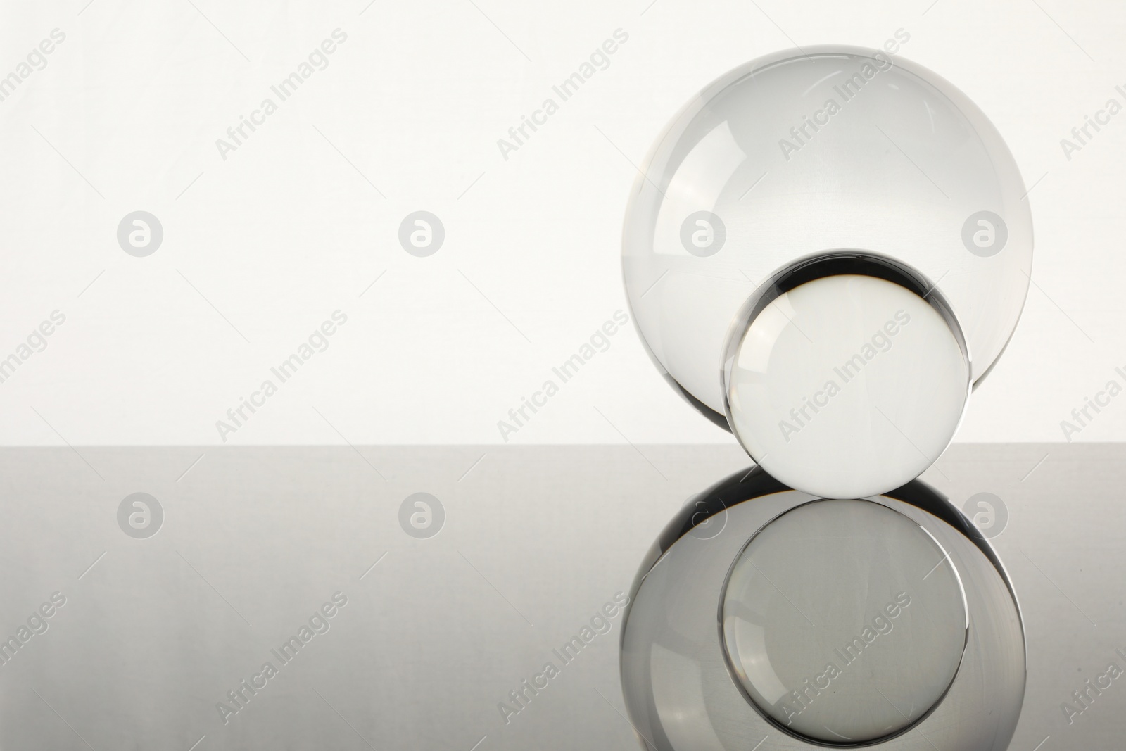 Photo of Transparent glass balls on mirror surface against light background. Space for text