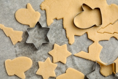 Photo of Raw Christmas cookies and cutters on baking parchment, top view