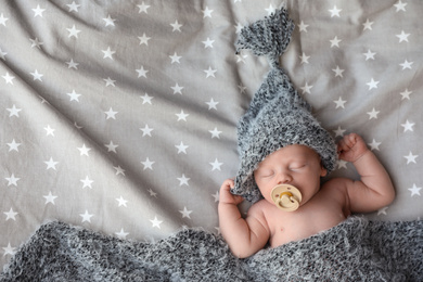 Photo of Cute newborn baby in warm hat sleeping on bed, top view. Space for text