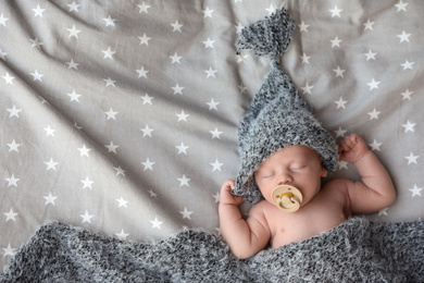 Cute newborn baby in warm hat sleeping on bed, top view. Space for text