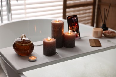 White wooden tray with burning candles and beauty products on bathtub in bathroom