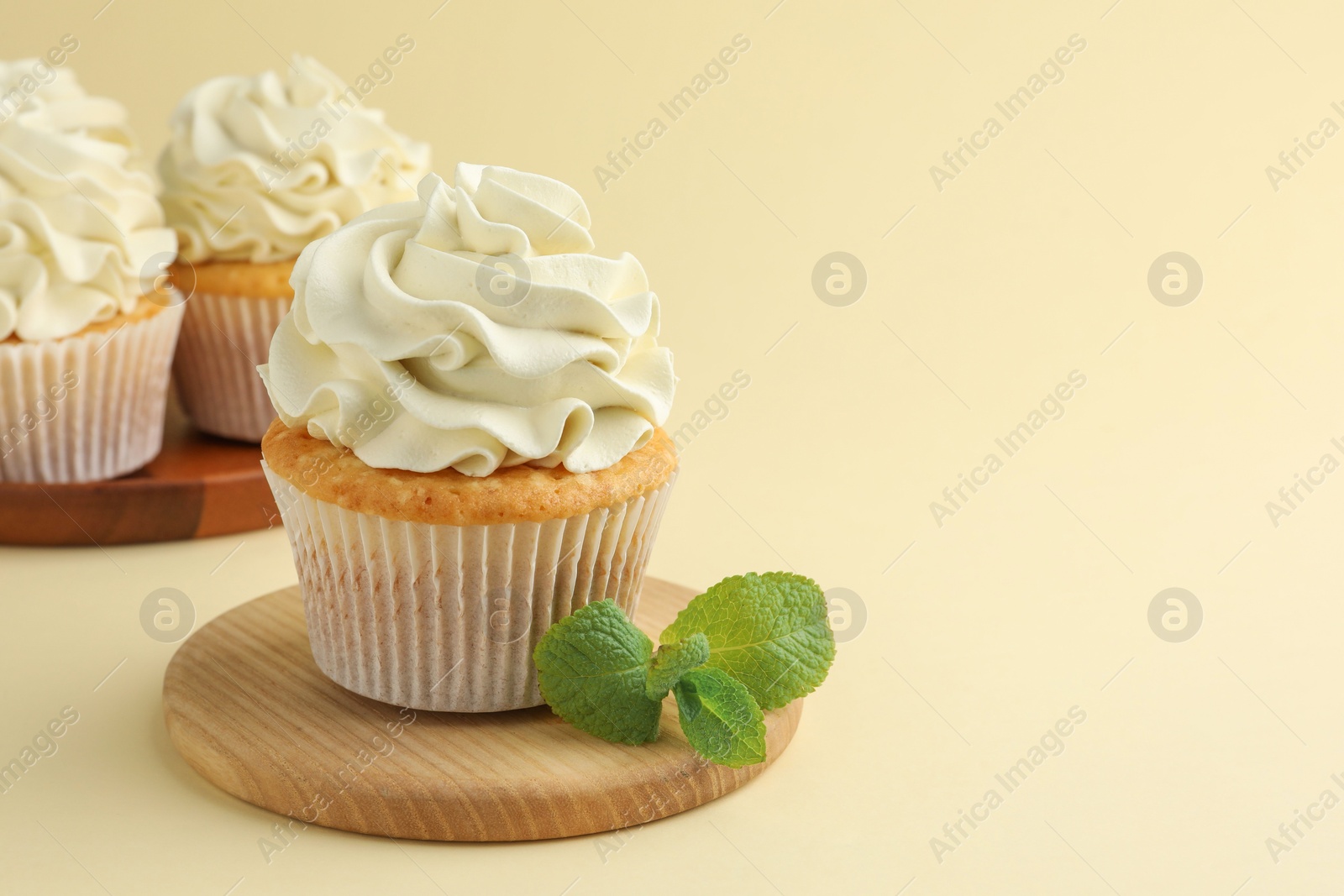 Photo of Tasty vanilla cupcakes with cream and mint on pale yellow background, space for text