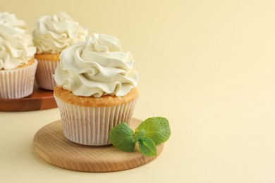 Tasty vanilla cupcakes with cream and mint on pale yellow background, space for text