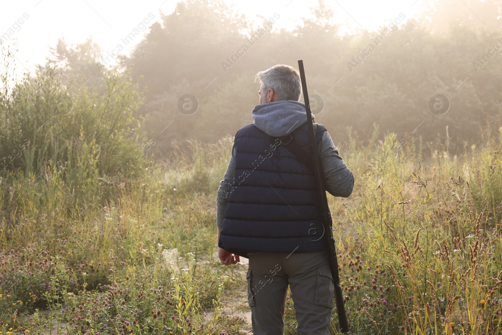 Photo of Man with hunting rifle outdoors, back view