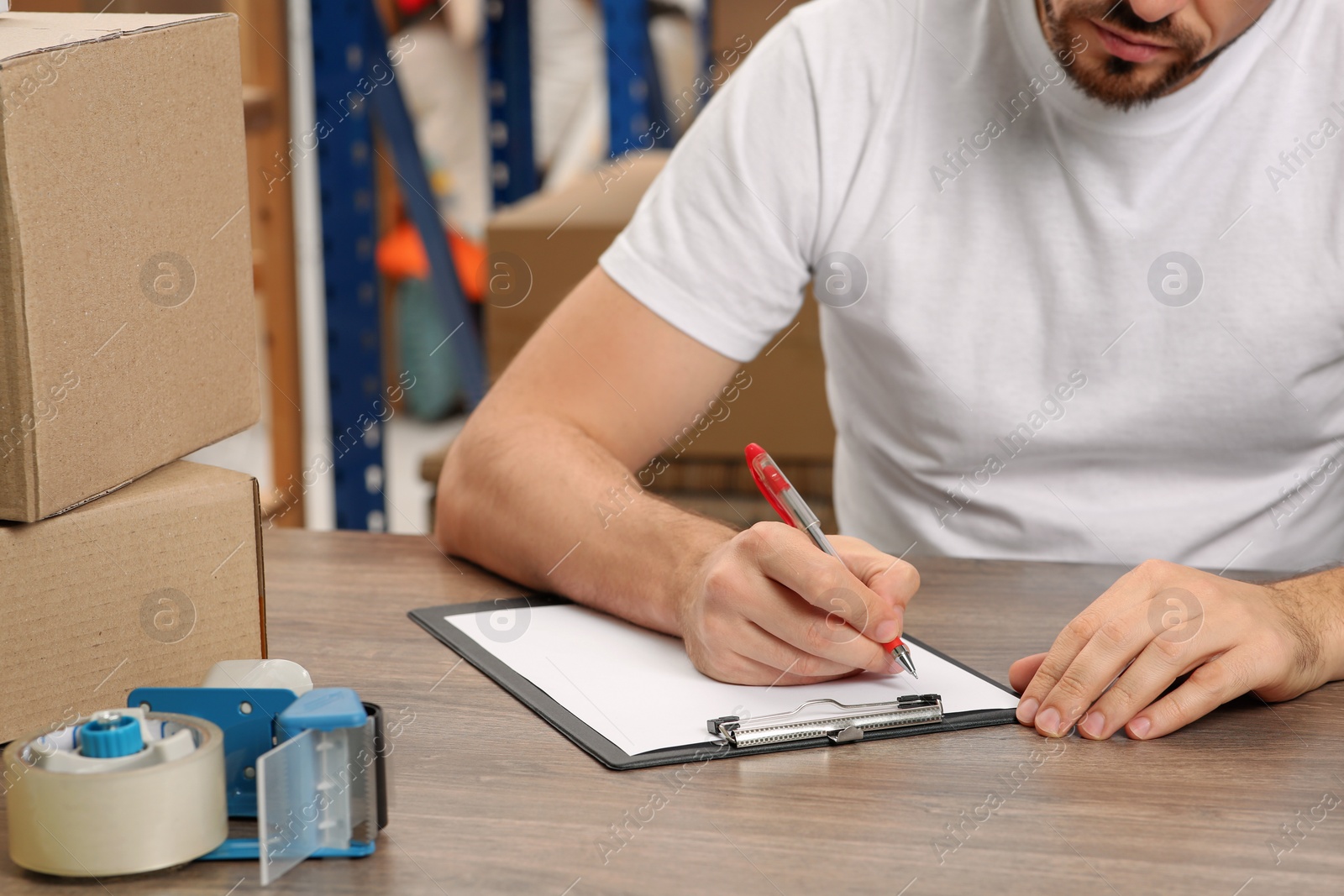 Photo of Post office worker with clipboard and parcels at counter indoors, closeup