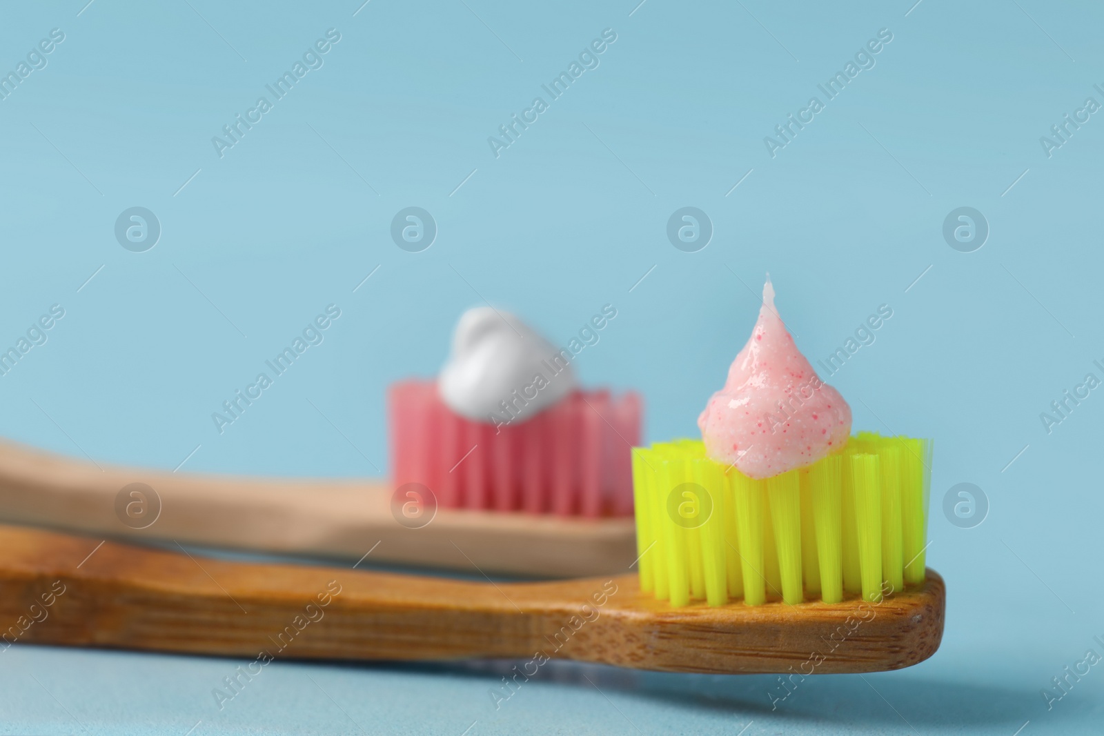 Photo of Wooden brushes with toothpaste on light blue background, closeup