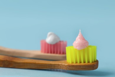 Photo of Wooden brushes with toothpaste on light blue background, closeup