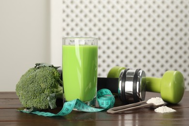 Photo of Tasty shake, broccoli, dumbbells, measuring tape and powder on wooden table. Weight loss