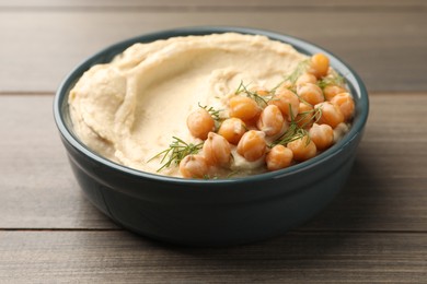 Photo of Bowl of tasty hummus with chickpeas and dill on wooden table, closeup