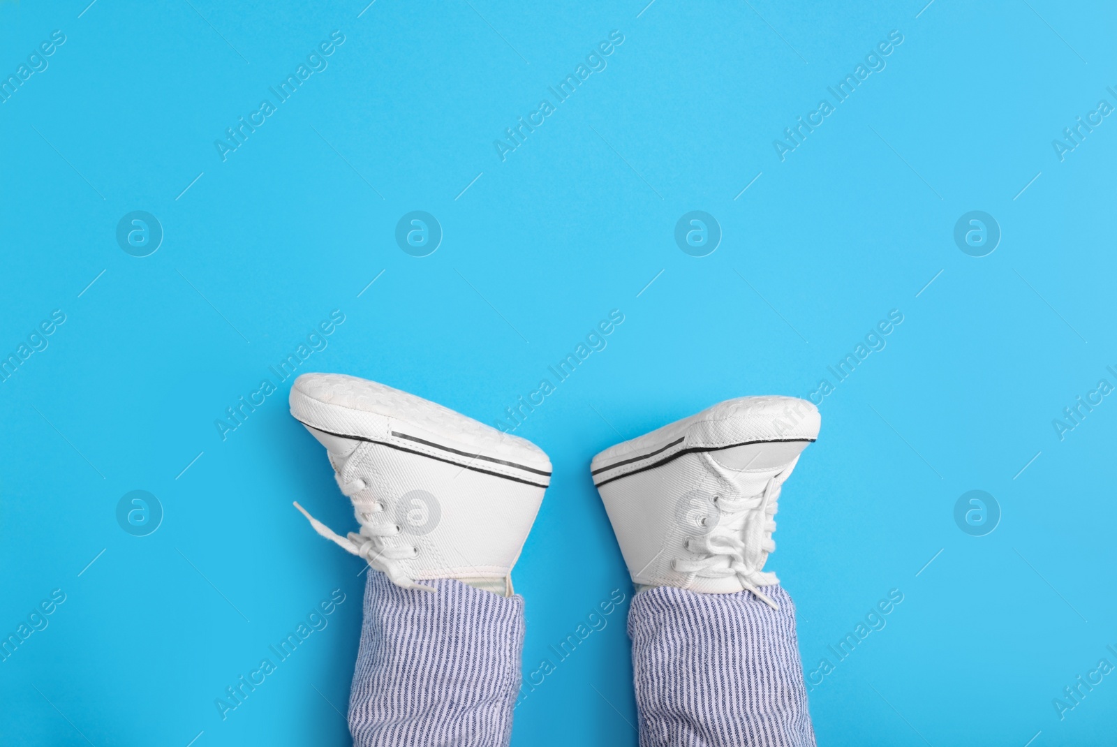 Photo of Little baby in stylish gumshoes on light blue background, top view. Space for text