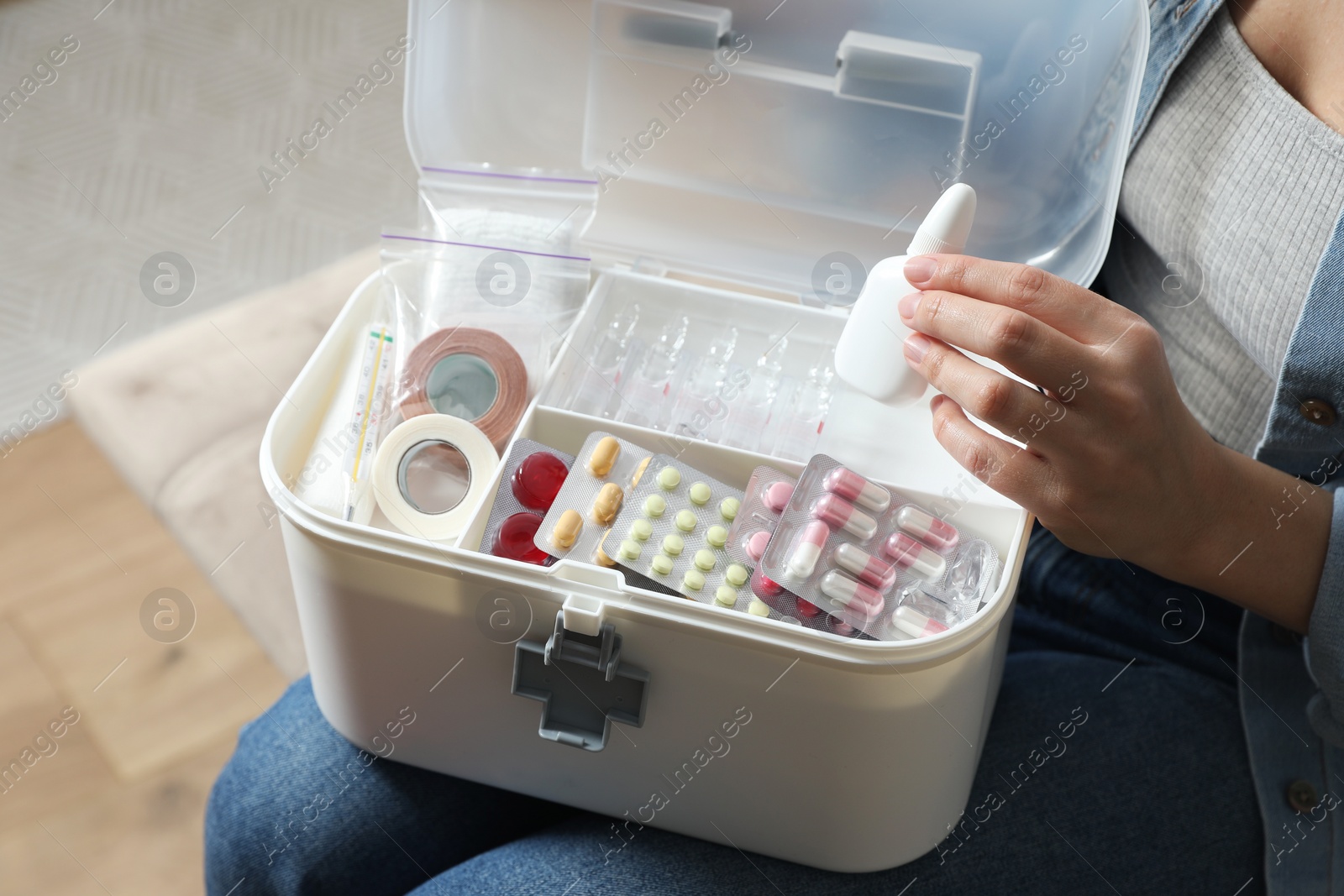 Photo of Woman putting medicament into first aid kit indoors, closeup