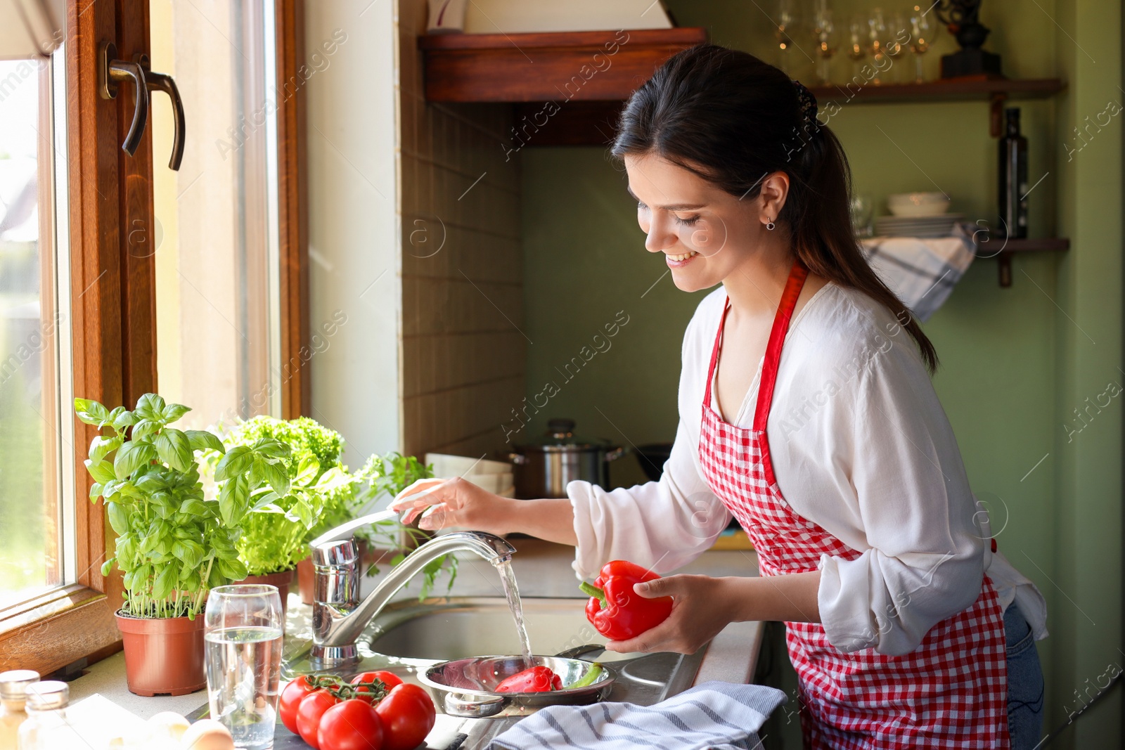Photo of Young woman washing fresh bell peppers in kitchen sink