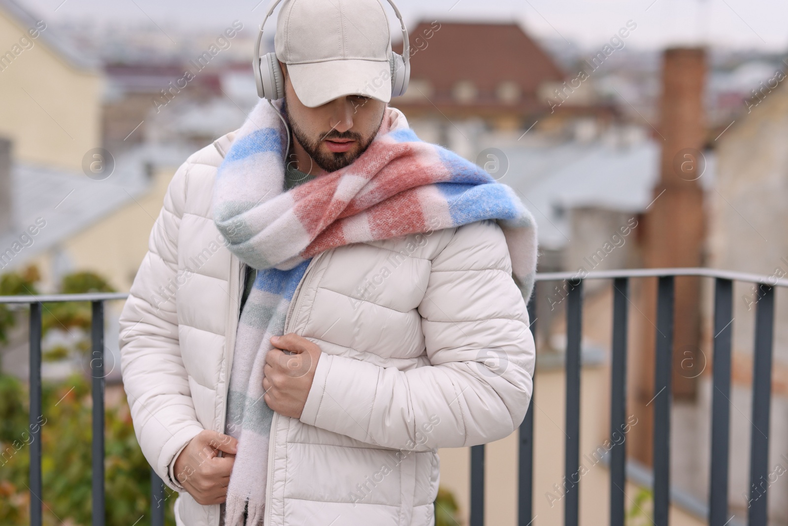 Photo of Handsome man in warm scarf and headphones outdoors