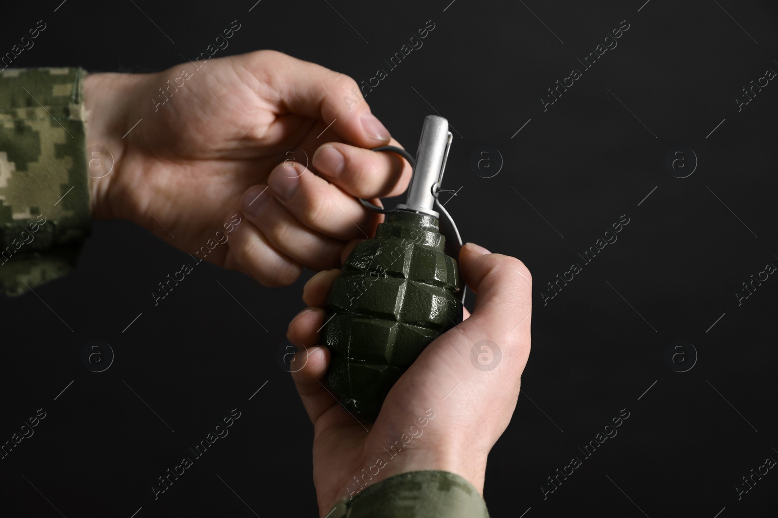 Photo of Soldier pulling safety pin out of hand grenade on black background, closeup. Military service