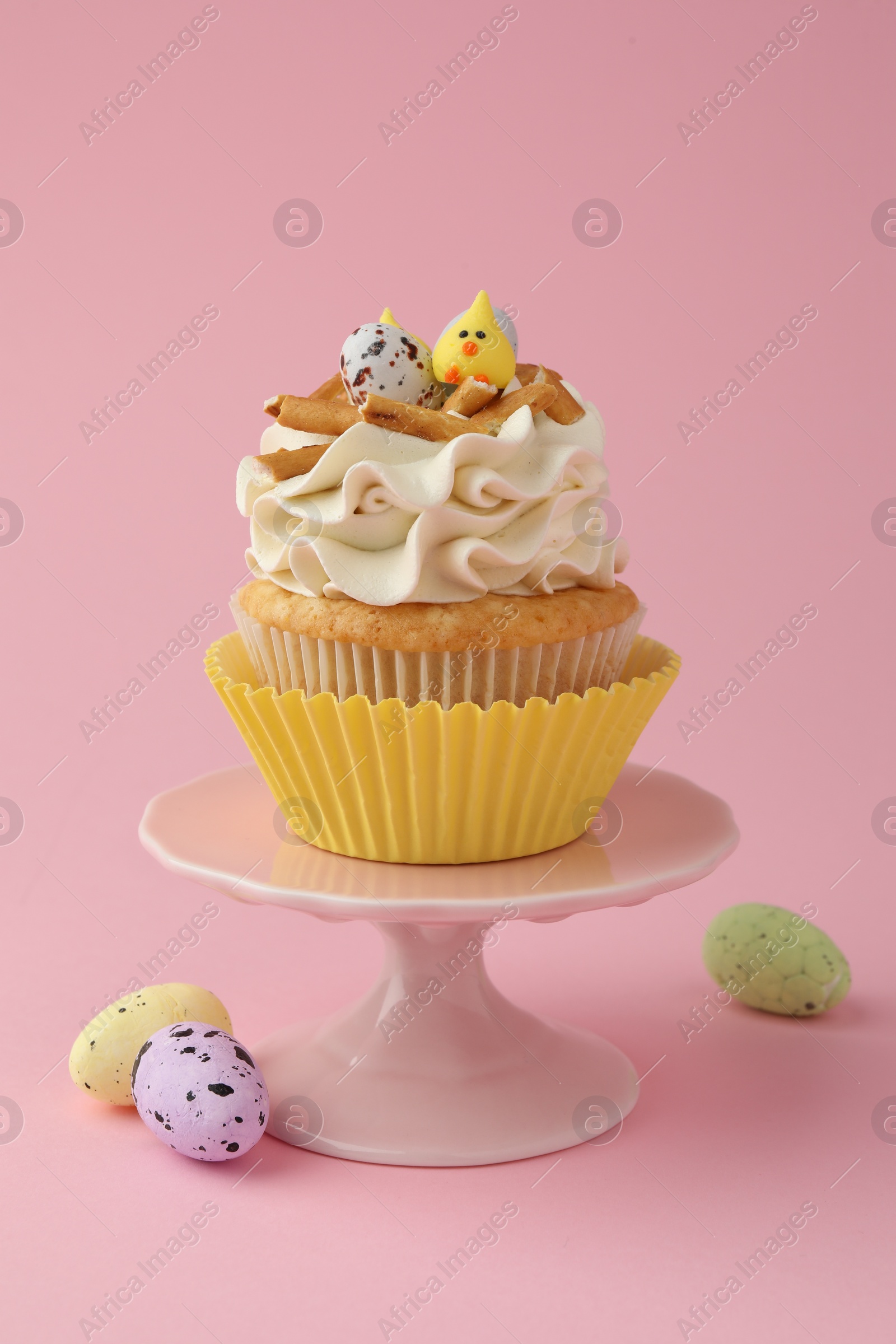 Photo of Tasty Easter cupcake with vanilla cream and candies on pink background