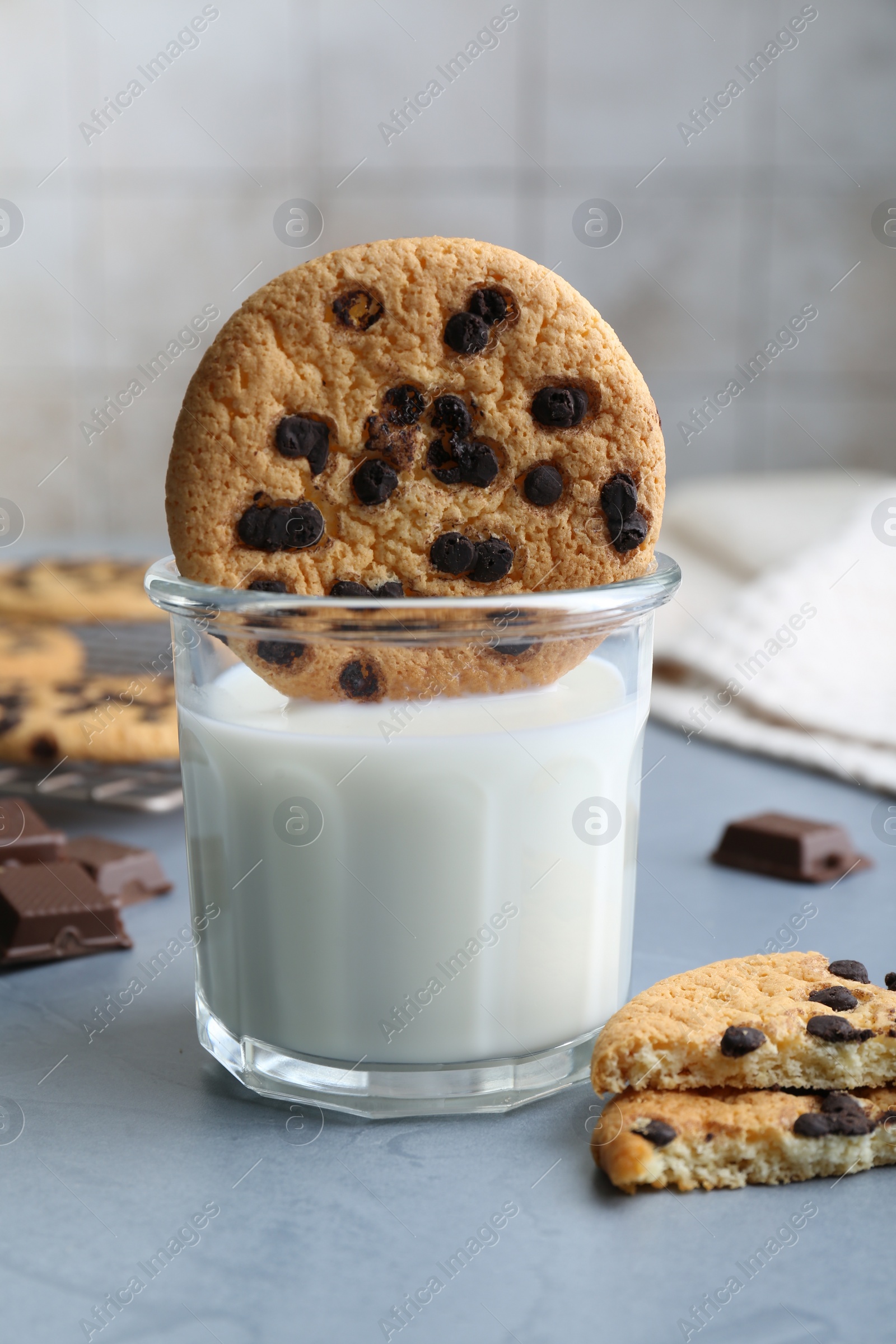 Photo of Delicious chocolate chip cookie dipped into glass of milk at grey table